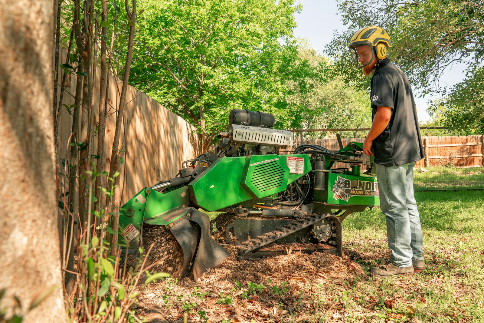 Example photo of a worker running a stump grinder beside a backyard fence